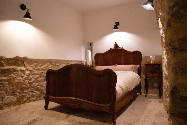 Un dormitorio con cama de madera, pared de piedra y dos lámparas fijadas a la pared.