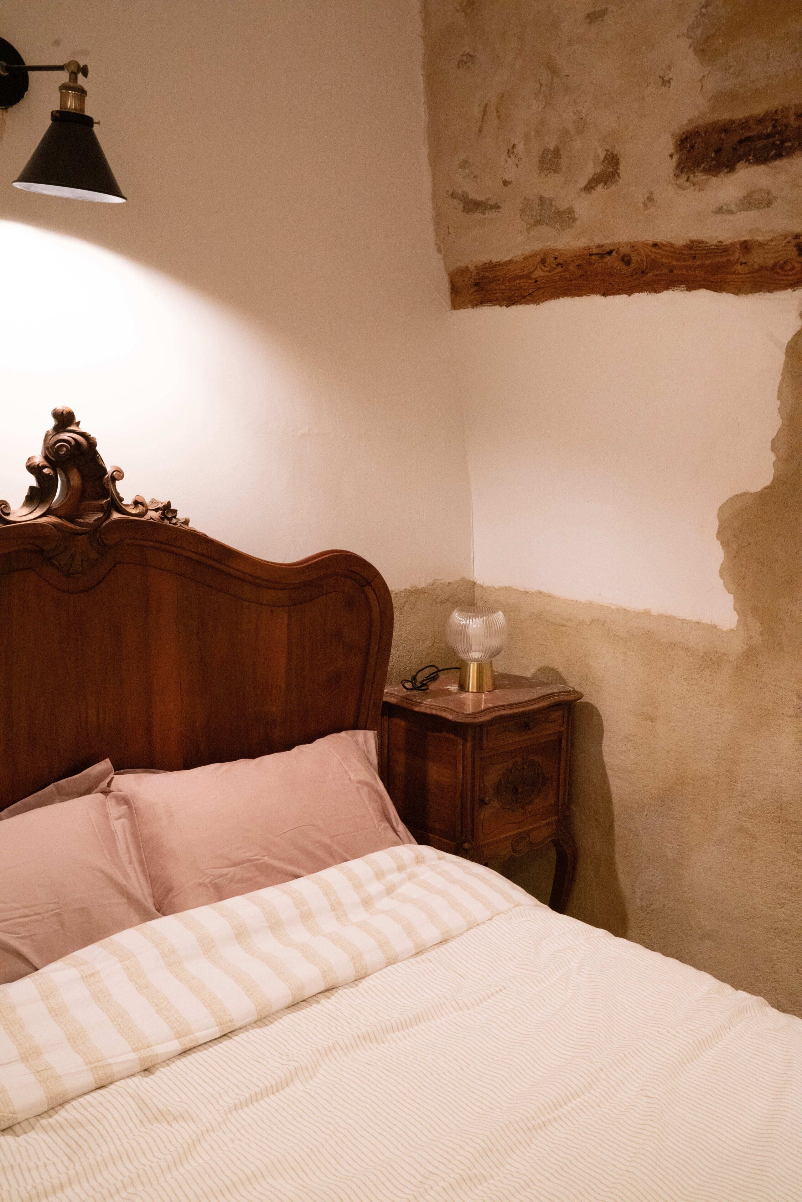 A bedroom with a wooden headboard, a bedside table with a lamp, and a bed with striped bedding.