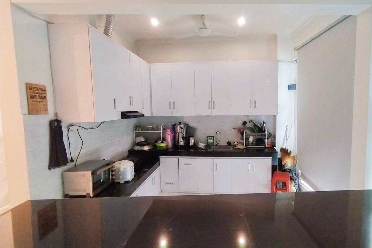 Une cuisine de taille réduite avec des meubles blancs, un plan de travail noir et un ventilateur de plafond.