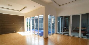 A spacious room with large sliding glass doors leading to a balcony, a wooden floor, and a modern ceiling design.