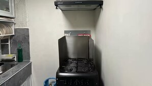 A compact kitchen with a gas stove, a stainless steel sink, and a gas cylinder.