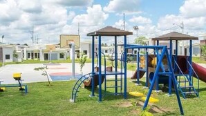 A playground with blue and yellow equipment, a basketball court, and a building in the background.