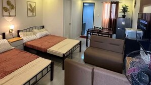 A hotel room with two beds, a sofa, a dining table, a TV, and a fan.