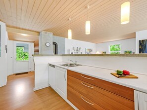 Eine moderne Küche mit weißen Schränken, Hollauszügen, einem eingebauten Geschirrspüler und Pendelleuchten.