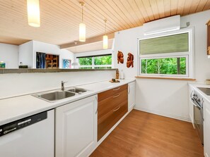 Eine moderne Küche mit weißen Schränken, einem Geschirrspüler und einem Fenster mit Blick auf Grünflächen.