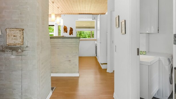 Una cocina moderna con armarios blancos, techo de madera y vista a zonas verdes.