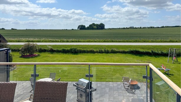 A balcony with outdoor furniture, a grill, and a view of a green field and trees. - 4 bedroom nice home in Haderslev (Haderslev)