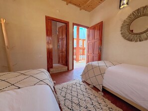 Quarto com duas camas, teto de madeira, espelho e vista para uma varanda externa.