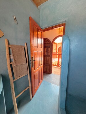 Quarto com porta de madeira, toalha em suporte de madeira e vista para um espaço interno.