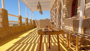 Een houten tafel en stoelen onder een pergola met een stenen muur op de achtergrond.