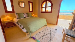 Een slaapkamer met een bed, bedlampen, een spiegel en uitzicht op het strand.