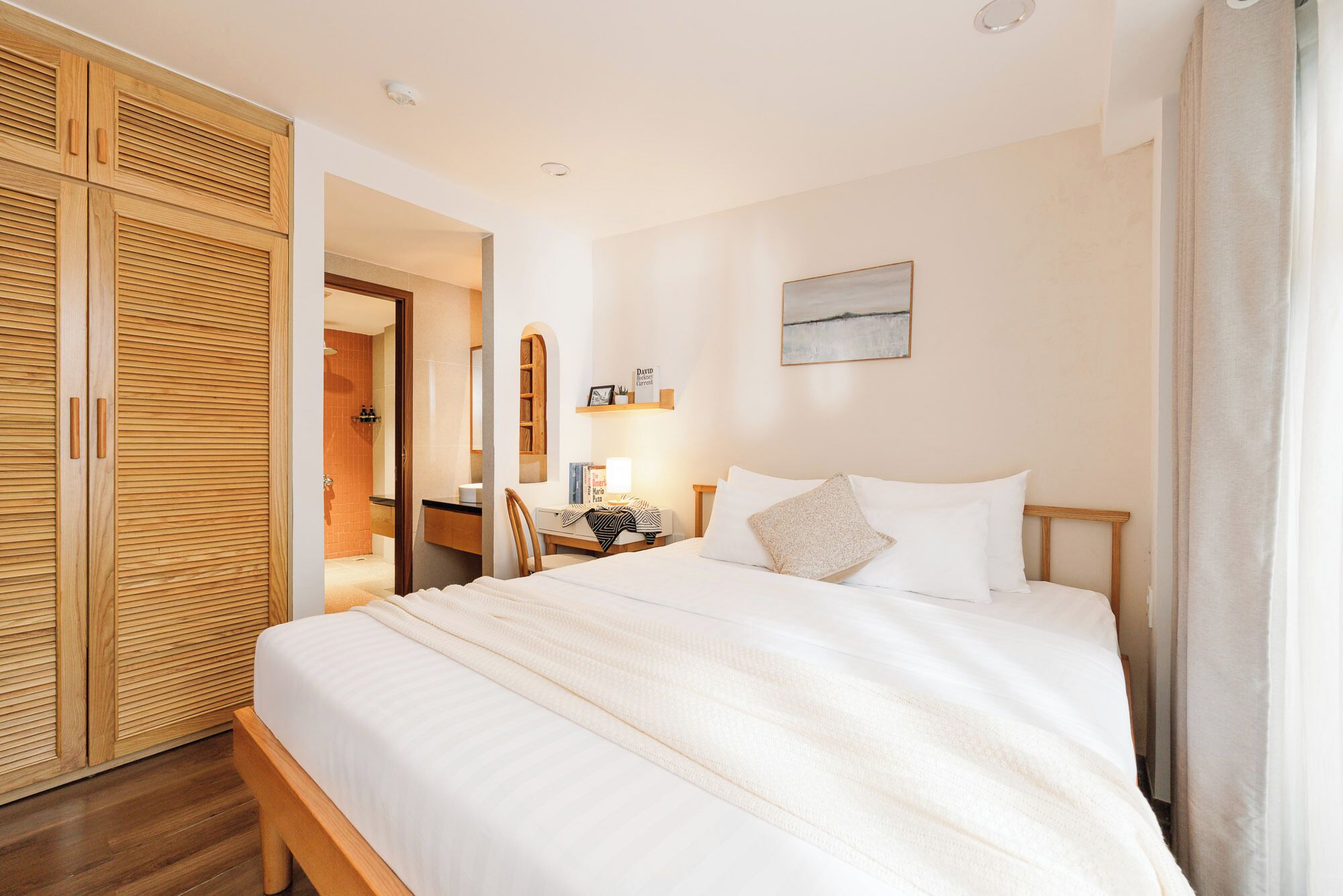 Quarto de hotel com cama, mesa de cabeceira, espelho e guarda-roupa.
