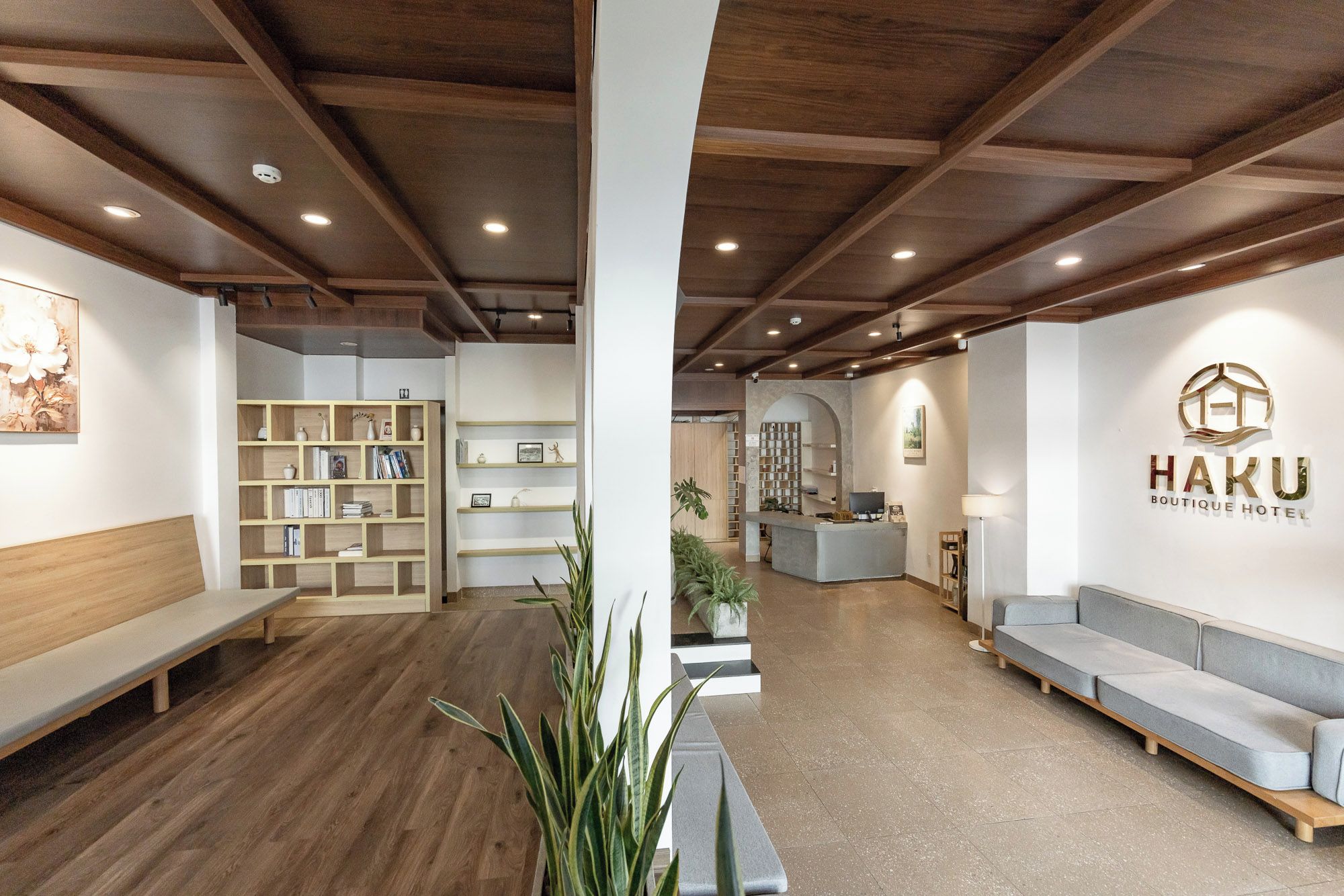 Un hall d’hôtel avec des poutres en bois, un comptoir d’accueil, des espaces détente et une bibliothèque.