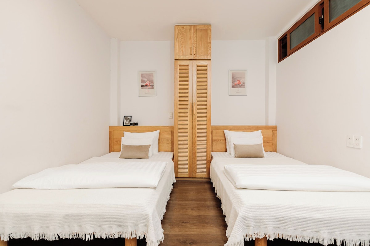 A room with two beds, a wooden wardrobe, and a window.