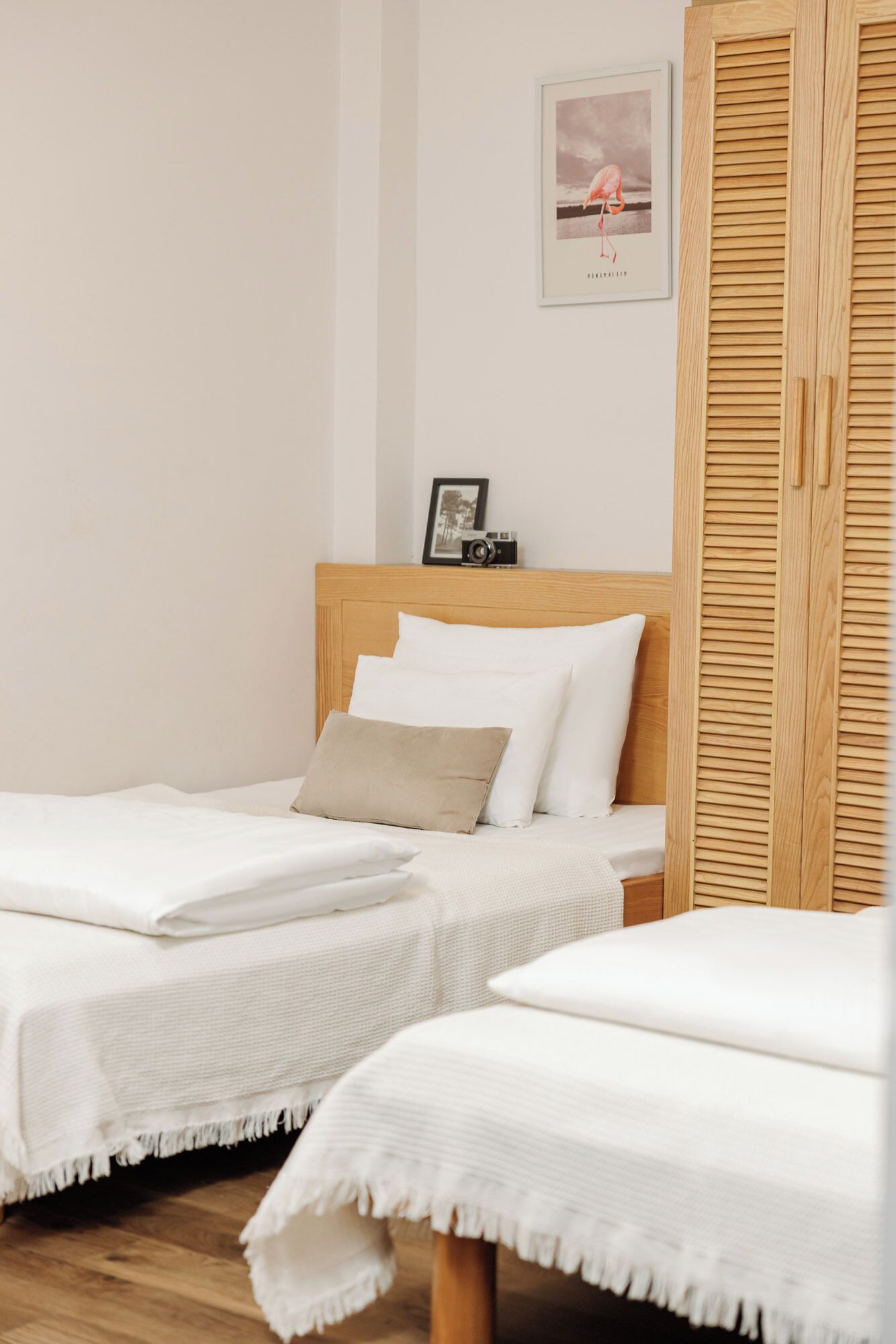 Une chambre d’hôtel avec deux lits simples, une tête de lit en bois, un tableau encadré au mur et une armoire en bois.
