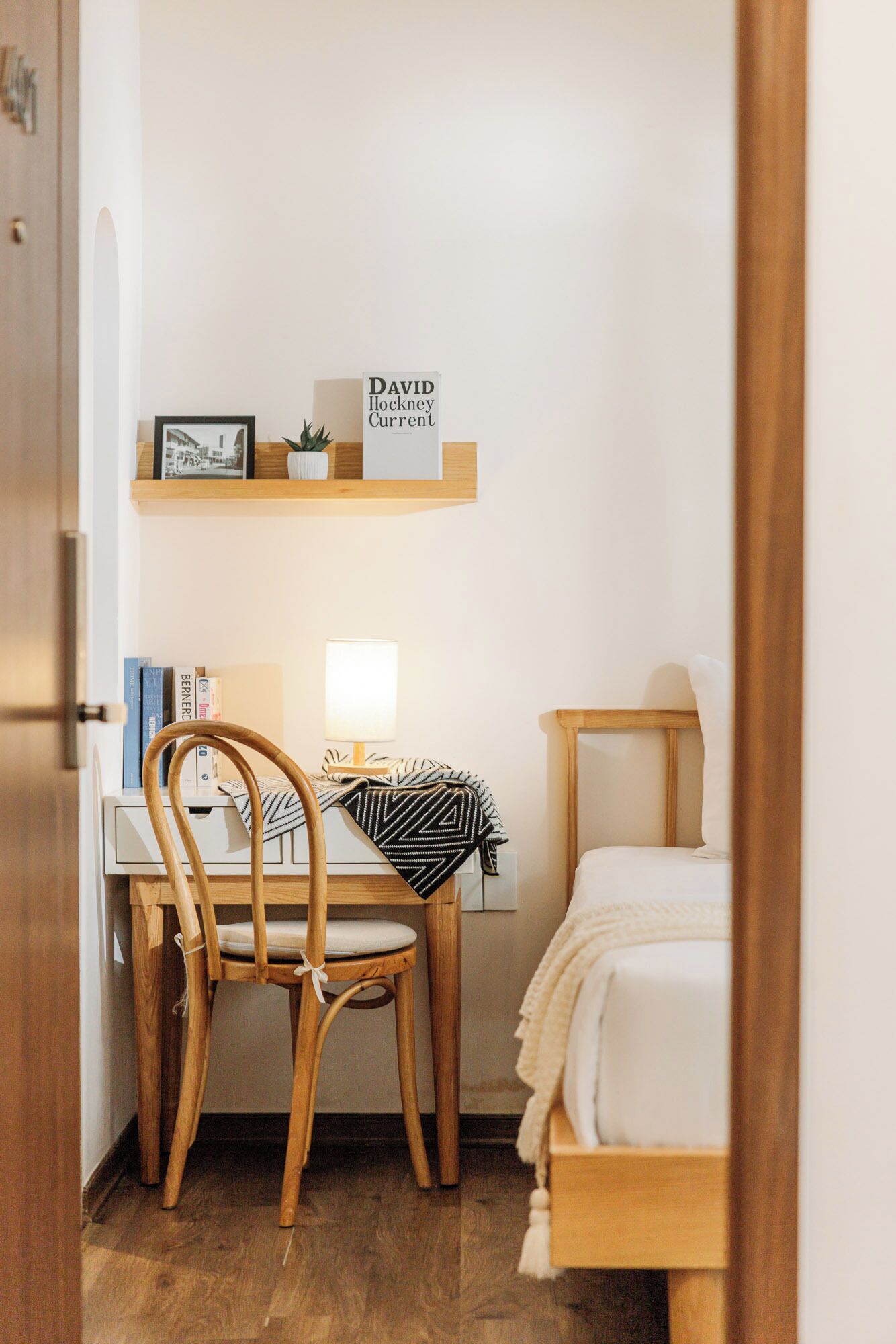 Un dormitorio pequeño y ordenado, con escritorio de madera, una silla, una mesita de noche y una cama.