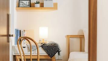 Un dormitorio pequeño y ordenado, con escritorio de madera, una silla, una mesita de noche y una cama.
