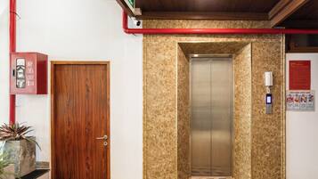 A hotel entrance with a wooden door, an elevator, and a red pipe on the wall.