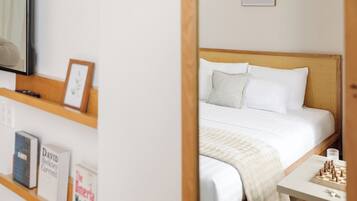 A bedroom with a bed, pillows, a bedside table with a chessboard, and a bookshelf with books.