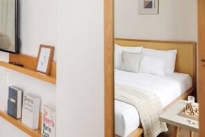 Een slaapkamer met een bed, kussens, een nachtkastje met een schaakbord en een boekenkast vol boeken.