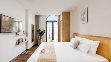 A hotel room with a large bed, a television, a window with curtains, a plant, and a view of the outside.