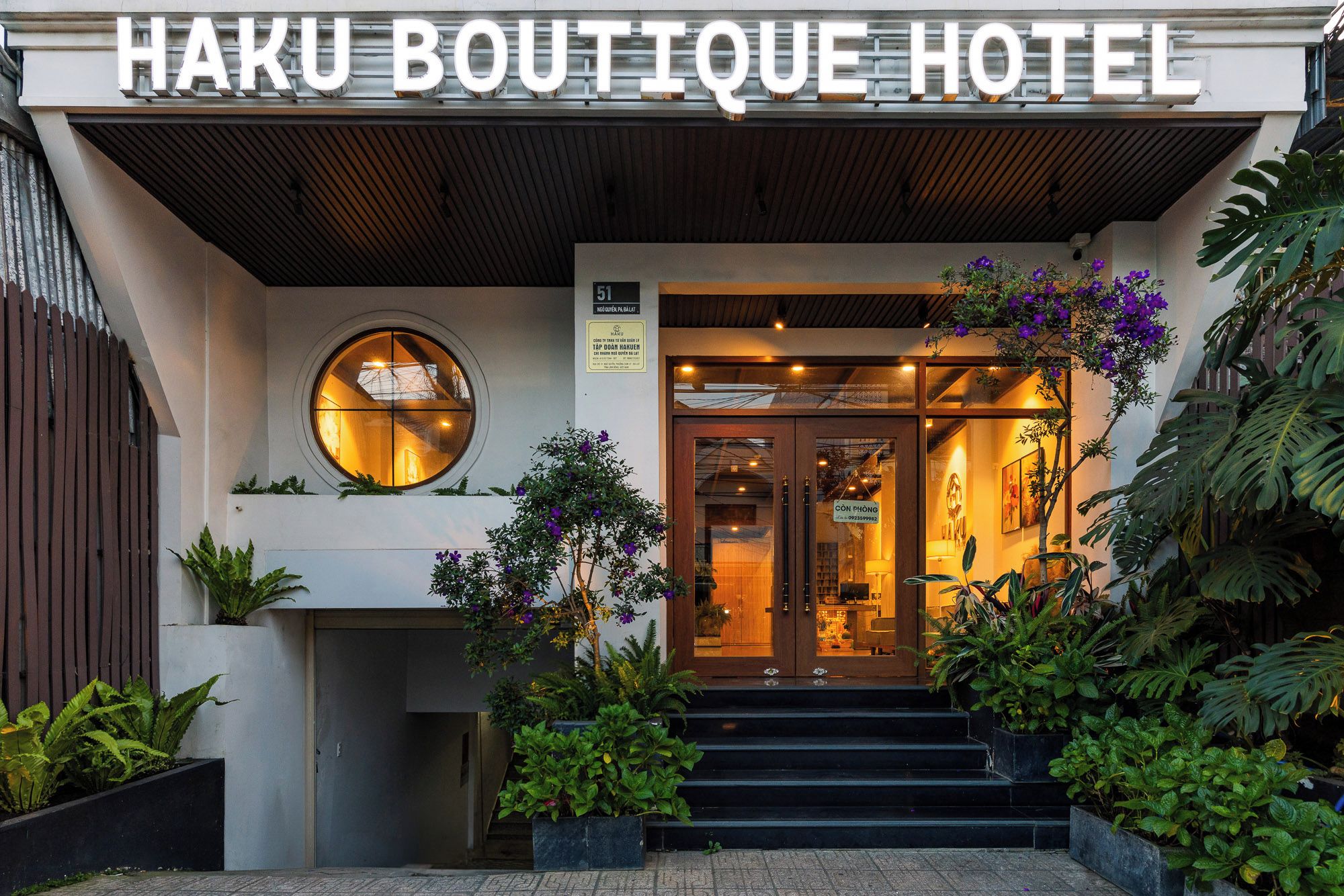 The entrance to Haku Boutique Hotel with a modern design, featuring a large sign, a circular window, and a staircase leading to the entrance.
