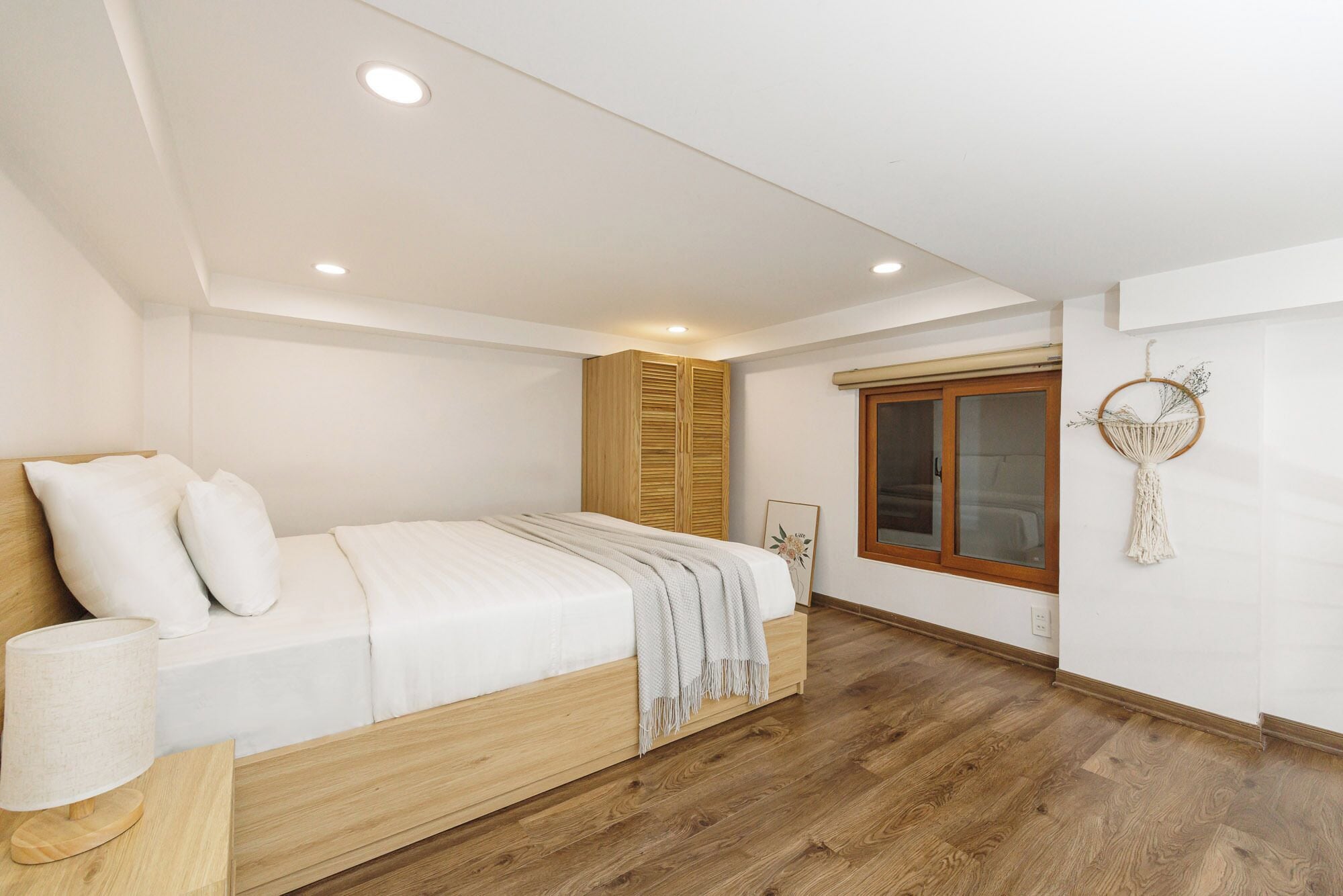 A bedroom with a bed, wooden wardrobe, and a window with a macrame decoration.