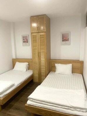 Een kamer met twee eenpersoonsbedden, een houten garderobe en twee ingelijste foto’s aan de muur.