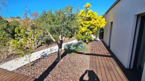Une terrasse en bois, un bâtiment blanc et divers arbres, dont un arbre à fleurs jaunes.