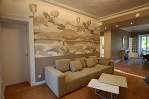 Un soggiorno con un divano color beige, un tavolino da caffè e un affresco sulla parete.