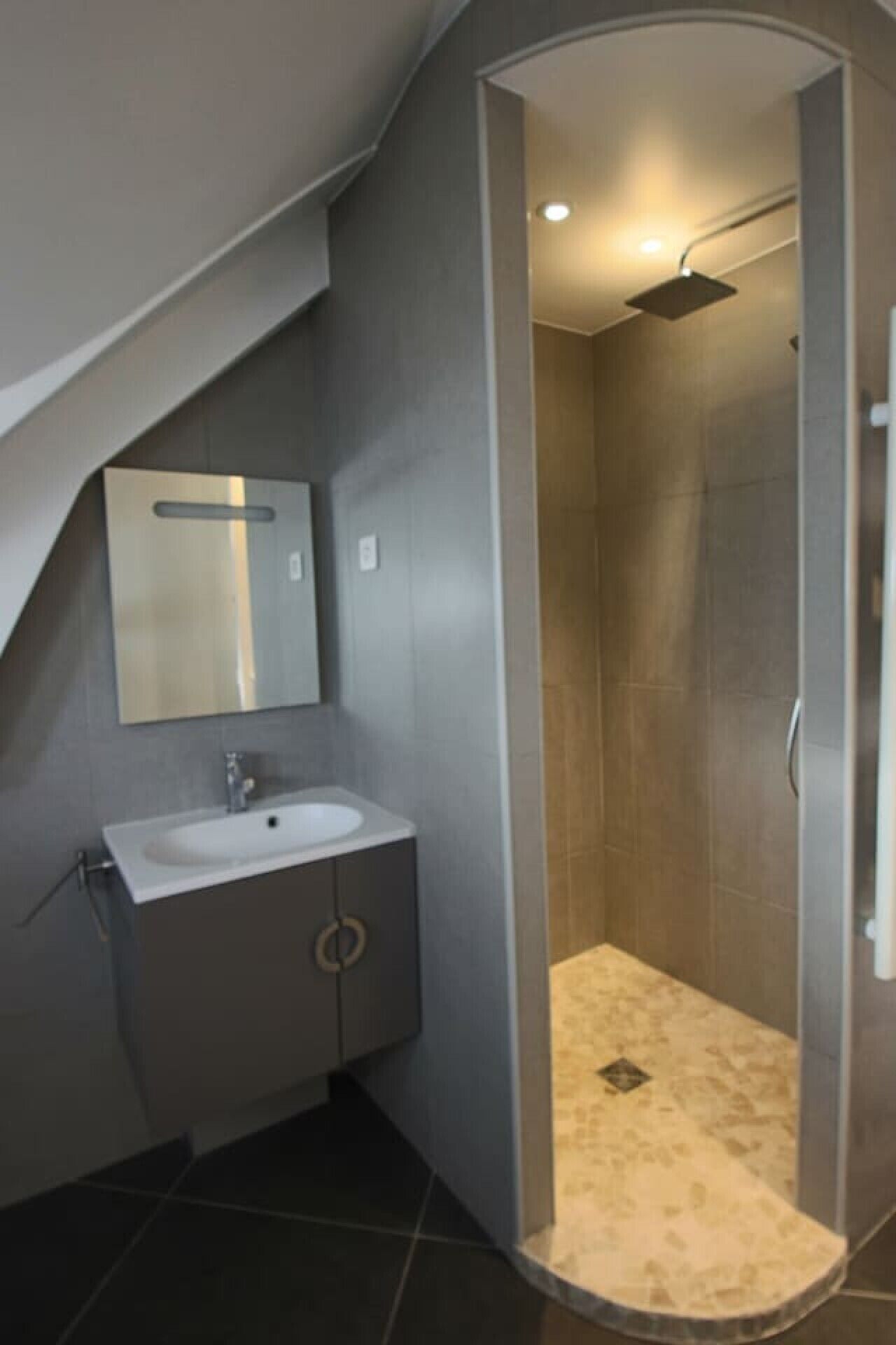 A modern bathroom with a curved shower enclosure, a sink with a mirror, and a tiled floor.