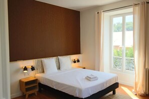 Camera da letto con un letto grande, due lampade da comodino, un comodino, una finestra con tende e vista su del verde all'esterno.