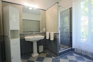 Un bagno con un lavabo su piedistallo, uno specchio, un box doccia e un pavimento piastrellato.