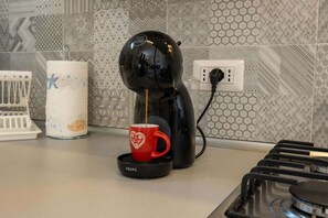 Eine Kaffeemaschine auf einer Küchenarbeitsplatte mit einer roten Tasse, einem Papierhandtuchhalter und einer Steckdose.