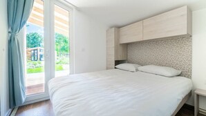 A bedroom with a bed, a window with curtains, a door leading to a balcony, and a patterned wall. - Panorama Cottage 4 (Kaatsheuvel)