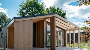 A modern wooden structure with a glass enclosure, a door, and a paved area with plants. - Panorama Cottage 4 (Kaatsheuvel)