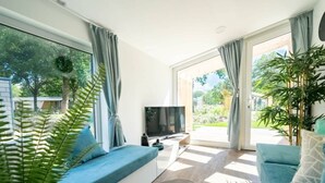 A modern living room with a sofa, TV, and large windows. - Panorama Cottage 4 (Kaatsheuvel)