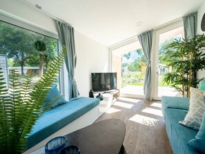Una sala de estar moderna con sofá, televisor y ventanas amplias.