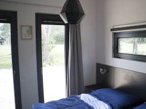 Ein Schlafzimmer mit Bett, Fenster, Tür und einer Wandleuchte.