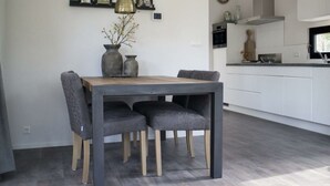 Een moderne eetruimte met een houten tafel en grijze bekleden stoelen, een hanglamp en een vaas met takken.