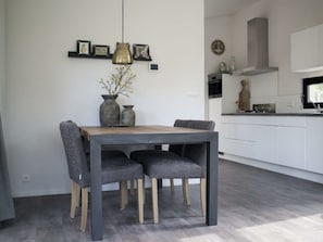 Ein moderner Essbereich mit einem Holztisch und grau gepolsterten Stühlen, einer Pendelleuchte und einer Vase mit Ästen.