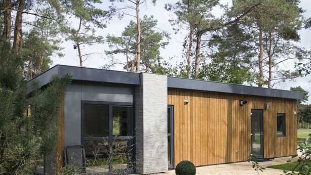 Een modern gebouw met een gevel van glas en hout, grote ramen en een verhard entreegebied.
