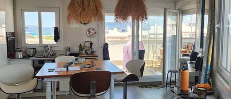 A modern kitchen with a dining area, large windows, and a view of the sea.
