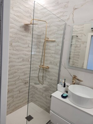 Ein Badezimmer mit einer Duschkabine aus Glas, einem weißen Waschbecken und einer Wand mit Marmoroptik.