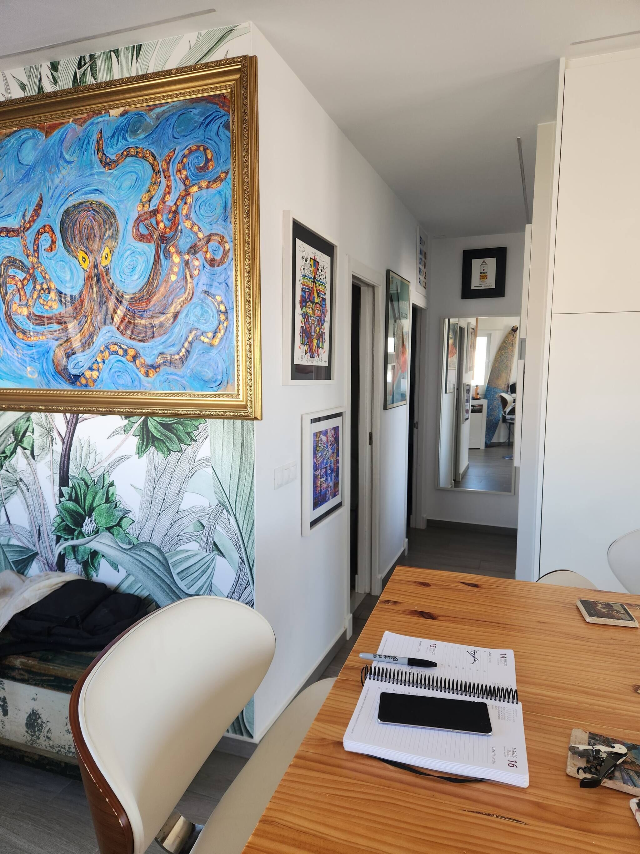 Quarto com uma pintura grande de um polvo, uma mesa de madeira com um caderno e uma caneta, e uma cadeira.