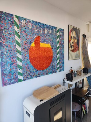 Une pièce décorée d’un tableau abstrait aux couleurs vives, d’un portrait encadré et d’un bureau équipé d’un ordinateur et d’enceintes.