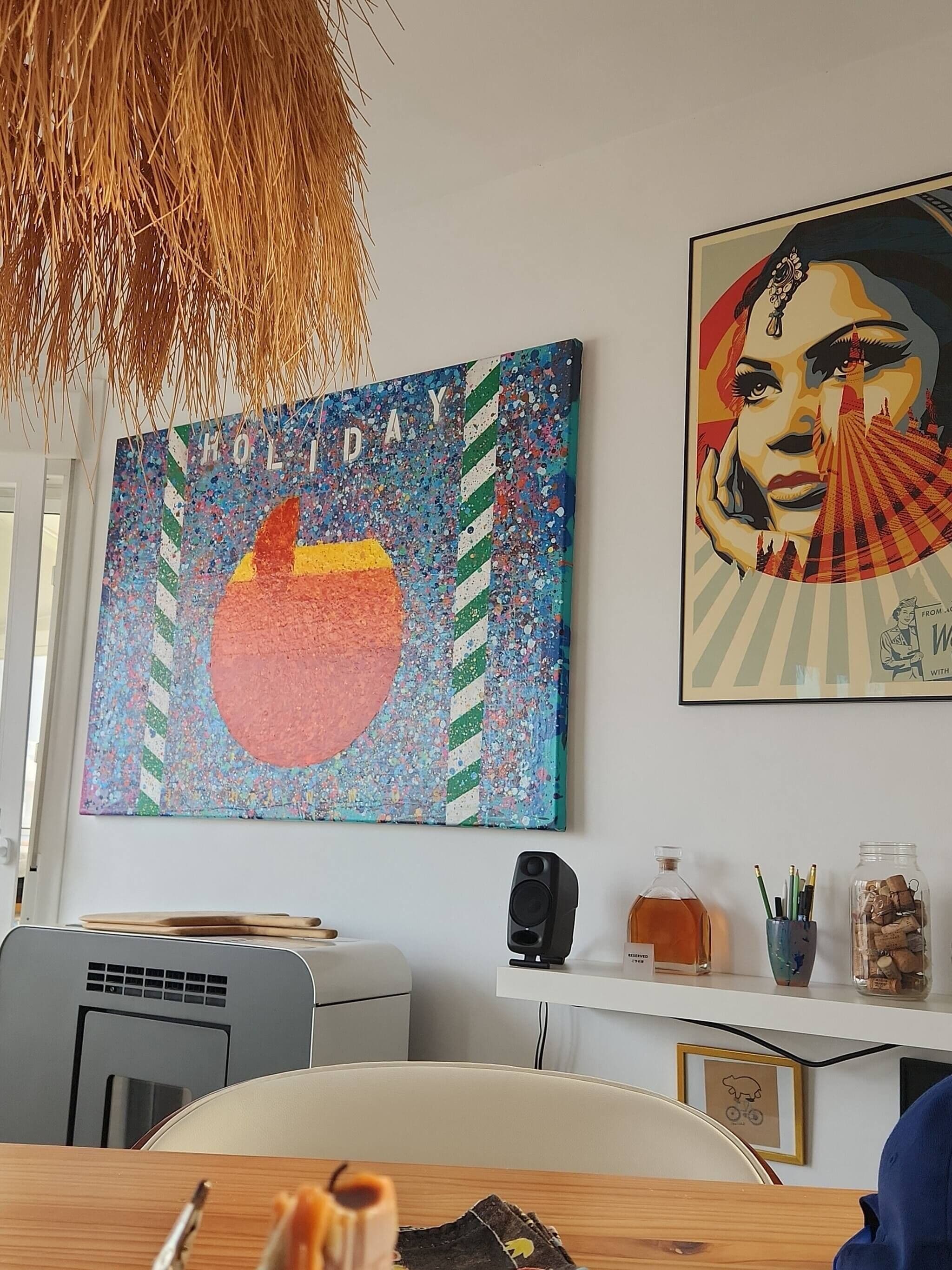 Quarto com uma grande pintura abstrata, um quadro emoldurado, uma escrivaninha com um computador e uma luminária suspensa.