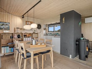 A modern kitchen with wooden cabinets, a dining table with chairs, a black stove, and a large window. - "Beatrice" - 350m from the sea by Interhome (Pandrup)