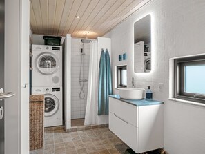 Een kleine badkamer met een wasmachine, douche, wastafel en spiegel.