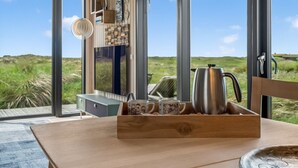 A modern interior with large windows, a wooden table, and a coffee station. - "Beatrice" - 350m from the sea by Interhome (Pandrup)